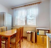 The kitchen of a 3-room apartment with a wooden decor floor, a dining table, and appliances.