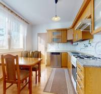 A kitchen in a 3-room apartment with a wood-patterned floor, wooden cabinets, and a table.