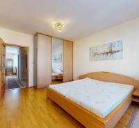 A bedroom in a 3-room apartment with a wood-patterned floor, a large wardrobe, and paintings.