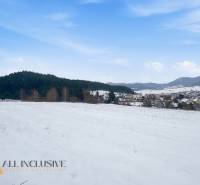 Snow-covered residential plots in Komjatná, surrounded by forests and mountains, with a view of the village.