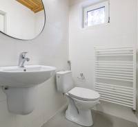 A bathroom in a family house with white tiles, a sink, a toilet, and a ladder radiator.