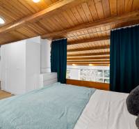 A bedroom in a family house with a wooden ceiling, a large window, and a floor with a wooden decor.