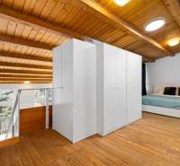 Attic bedroom in a family house with a wooden ceiling, floor with a wooden decor, and a bed.