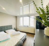 Bedroom in a three-room apartment with wood-patterned flooring and large windows.