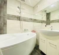 A bathroom in a 3-room apartment with a bathtub, sink, and tiles in light tones.