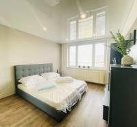 A bedroom in a three-room apartment with a wood-patterned floor and a large window.
