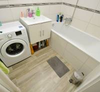 A bathroom in a 2-room apartment with a bathtub, washing machine, and a floor with a wooden decor.