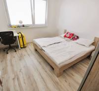 Bright bedroom in a 2-room apartment with a bed, a desk, and a floor with a wooden decor.