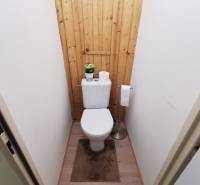 A toilet with a toilet bowl, wooden paneling, and a floor with a wooden decor in a 2-room apartment.