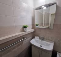 Bathroom in a 2-room apartment with a sink, mirror, and tiles in neutral shades.