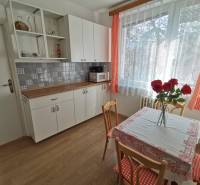 A kitchen in a 2-room apartment with a wooden decor floor and red curtains.