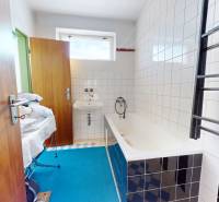 A bathroom in a family house with a bathtub, white tiles, and a blue carpet.