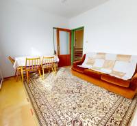 A room in a family house with a brown sofa and a dining table, a carpet, and curtains.