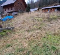 Land in Oščadnica designated for residential use with visible wooden structures on sloping terrain.