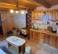 Interior of a cabin with wooden decor, kitchen unit, wood-burning stove, seating area.