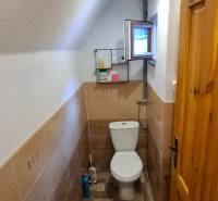 Toilet in a cabin with a wooden decor floor, storage shelves above the toilet.