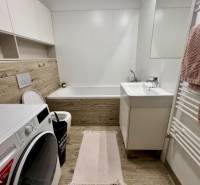 Bathroom in a 2-room apartment with a bathtub, washing machine, and floor with wood decor.