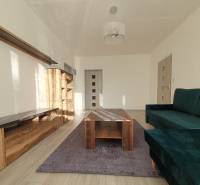Living room in a three-room apartment with a sofa, wardrobe, and table on a wooden decor floor.