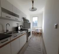 A kitchen in a 3-room apartment with a wooden decor floor and white furniture.