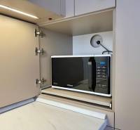 A microwave in a kitchen cabinet with a wooden floor in a 2-room apartment.