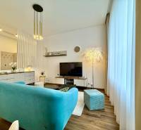 Living room of a two-room apartment with a turquoise sofa, light-colored wall, and floor with a wood decor.