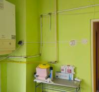 A bathroom in a family house with green walls, a boiler, and a shelf with supplies.