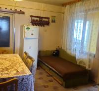 A kitchen in a family house with a tablecloth on the table, a sofa, and a refrigerator.