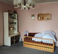 A room with a bed, shelves with dishes, and a hanging light fixture in a family house.
