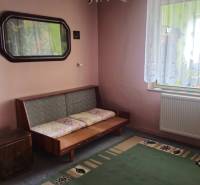 A room in a family house with a sofa, a green carpet, and an ornamental curtain.