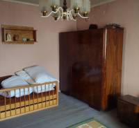 A room in a family house with a bed, a wardrobe, and a chandelier, the walls are light pink.