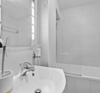 A bathroom in a 2-room apartment with a bathtub, mirror, and sink.