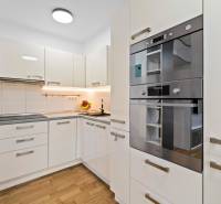 A kitchen in a 2-room apartment with glossy white cabinets and a floor with a wood decor.