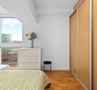 A bedroom in a two-room apartment with a wooden decor floor, wardrobes, a dresser, and a bed.