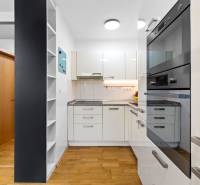 A kitchen in a 2-room apartment with white cabinets, appliances, and a wooden decor floor.