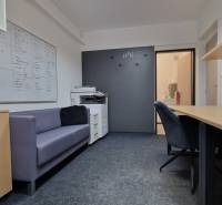 Offices with a sofa, white cabinets, a dark wall, and a floor with a wood decor.