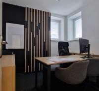 Offices with a desk, chairs, and a prominent wall with wooden slats, with light from the windows.