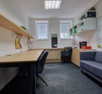 The interior of an office with desks, shelves, and chairs on a carpeted surface.