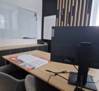 Office with a whiteboard, desk, computer, and decorative wall, equipped with comfortable chairs.