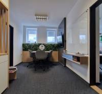 An office with a dark carpet, a whiteboard, and windows, providing a pleasant working environment.