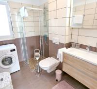Bathroom in a 3-room apartment with a washing machine, shower, and toilet, floor with wooden decor.