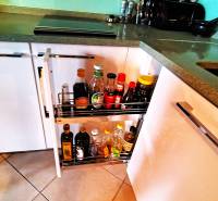 A kitchen cabinet with a pull-out organizer full of bottles and spices in a 2-room apartment.