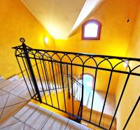 A staircase in the interior of a 2-room apartment with orange walls and wrought iron railing.