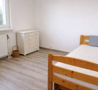 A room in a 3-room apartment with a wooden decor floor, a bed, and a dresser.