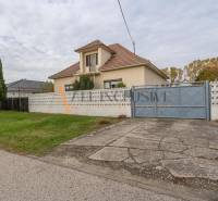 A family house in Veľké Dvorníky with a large garden, trees, and a concrete walkway.