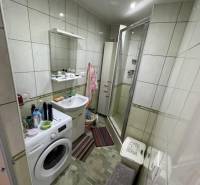 A bathroom in a 4-room apartment with a washing machine, shower corner, and tiles.