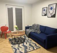 Living room in a three-room apartment with a blue sofa, a red armchair, and a wooden decor floor.