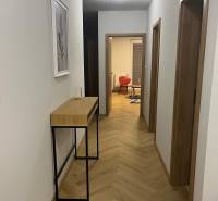 A hallway in a 3-room apartment with a wooden decor floor and furniture against the wall.