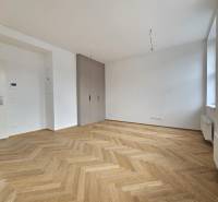 A spacious room in a one-bedroom apartment with a wooden decor floor and large windows.