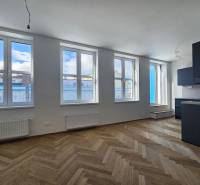A one-bedroom apartment with a wooden decor floor and a black kitchen unit.