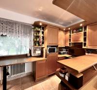 A kitchen in a family house with wooden cabinets and decor, tiled floor, flowers on the shelf.